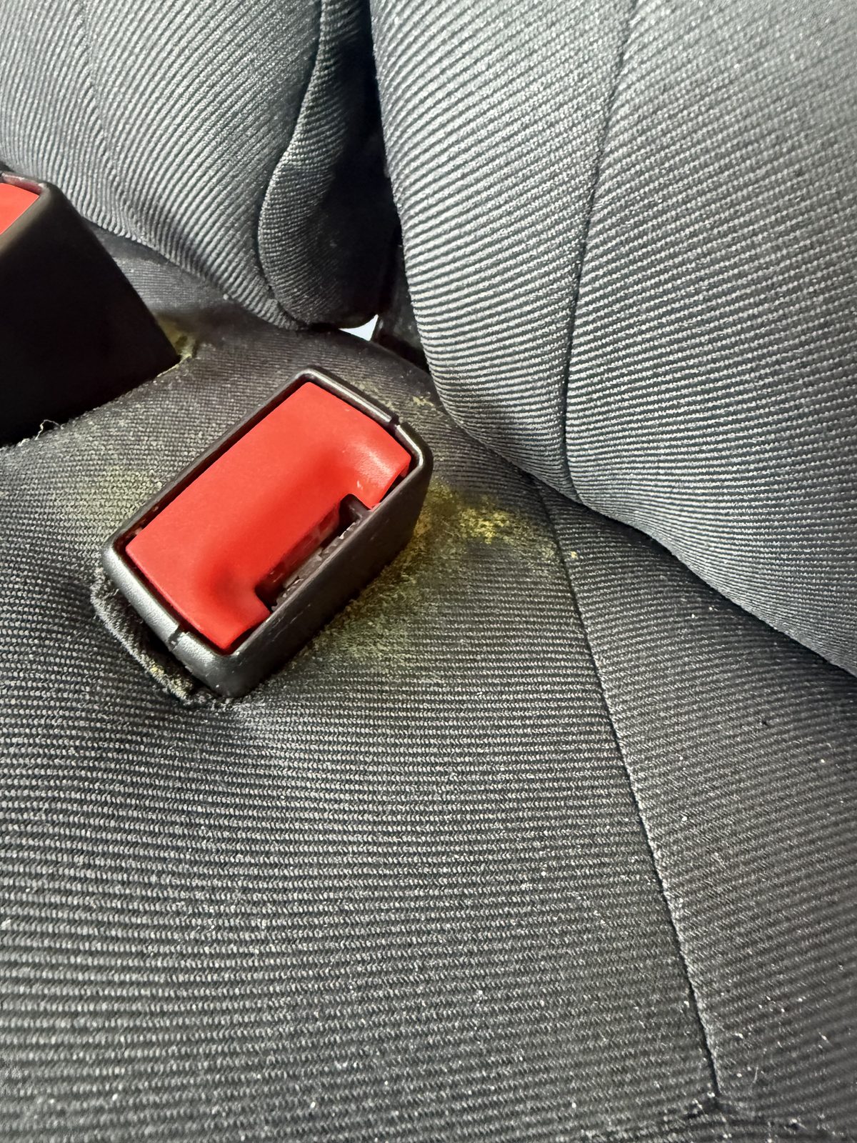 Yellow mildew spot on a fabric seat near the seatbelt buckle before cleaning